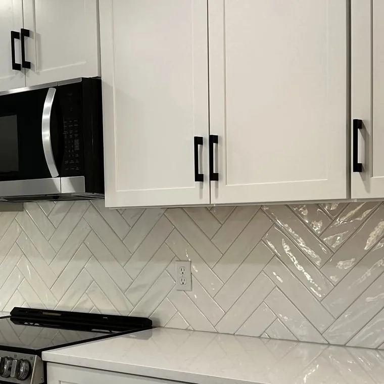 Herringbone tile backsplash running up to the underside of white cabinets