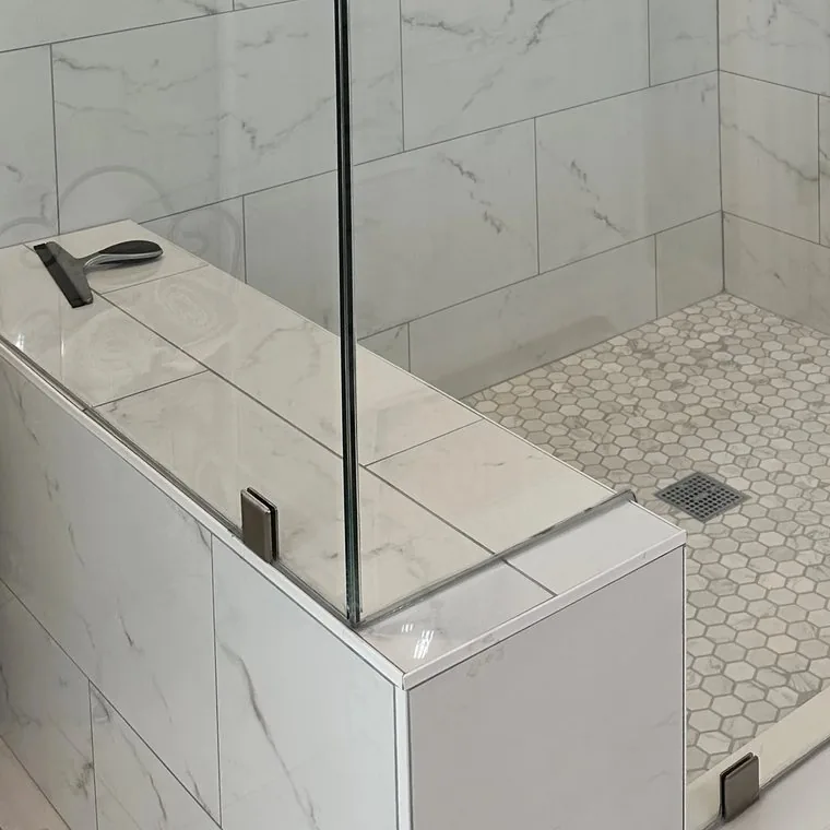 A marble shower curb with a hex mosaic pan and frameless glass