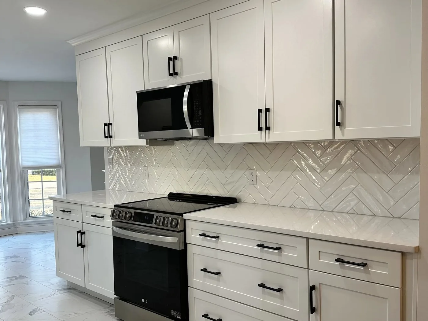 A white kitchen with a herringbone tile backsplash, marble-look floor tile and a stainless range