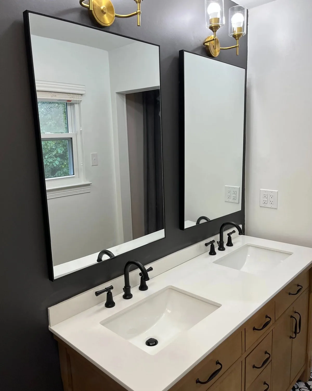 A bathroom with two black-framed mirrors and brass sconces on a dark painted wall