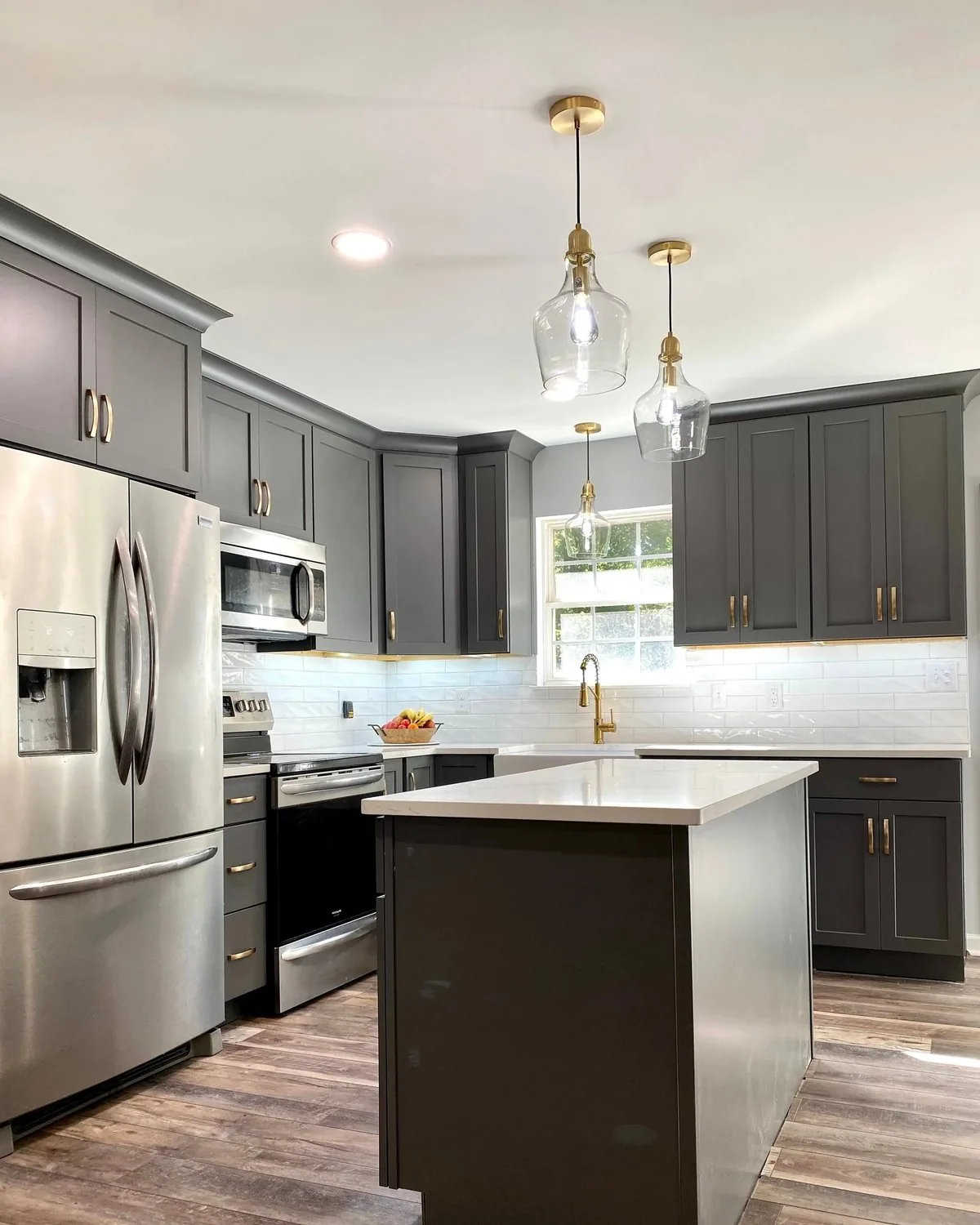 A gray kitchen with glass pendants over the island and stainless appliances