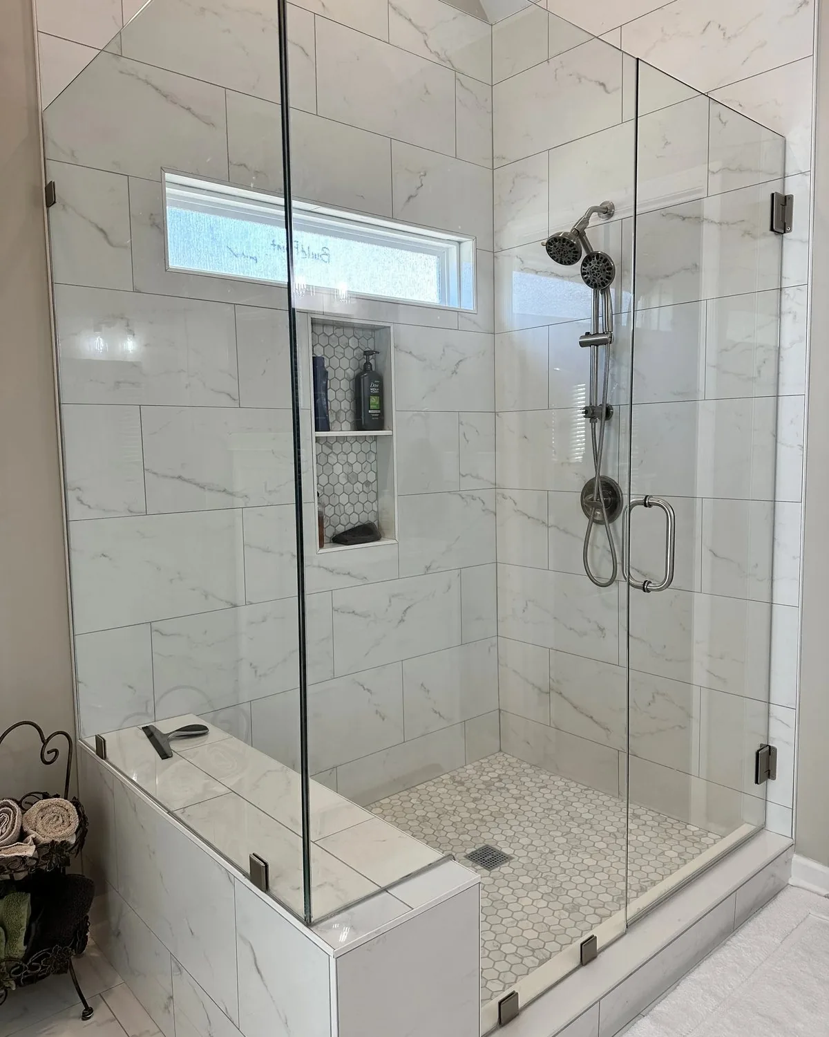 A glass shower with a marble curb, marble walls and a hex mosaic pan